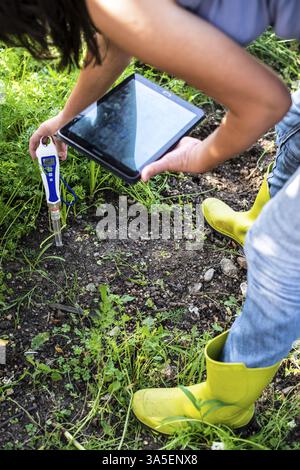 PH-Messgerät im Boden. Messen Sie den Boden mit einem digitalen Gerät und einem Tablet. Eine Farmerin im Garten. Konzept für neue Technologien in der Landwirtschaft Stockfoto