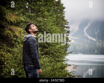 Schöner Yung-Mann, der auf dem Hintergrund des Waldes am Ufer des Sees steht und wegblickt Stockfoto