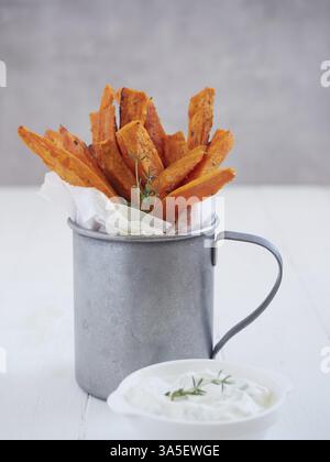 Gebratene Süßkartoffelstäbchen als Pommes frites in einer Metalltasse mit Joghurtsauce und Thymian Stockfoto