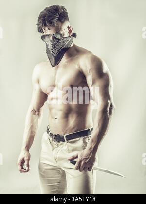 Schöner muskulöser junger Mann mit Maske über dem Gesicht als Räuber oder Räuber Stockfoto