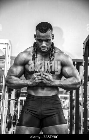 Attraktive Hunky schwarzen männlichen Bodybuilder Bodybuilding Pose im Fitness-Studio mit Eisenketten über Schultern zu tun Stockfoto