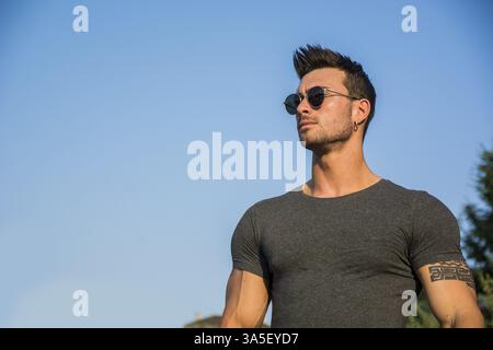 Schöner muskulöser Mann mit Tattoo, der draußen vor blauem Himmel posiert Stockfoto