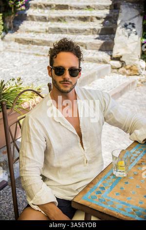 Porträt von stilvollen gut aussehender Mann in Sonnenbrille mit Flasche Wasser am Tisch im café Stockfoto