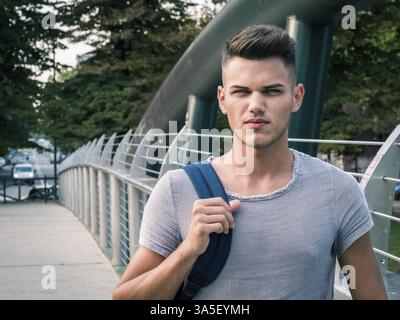 Gutaussehenden jungen Mann zu Fuß in der Stadt mit Rucksack auf den Schultern, das Tragen von T-Shirts Stockfoto