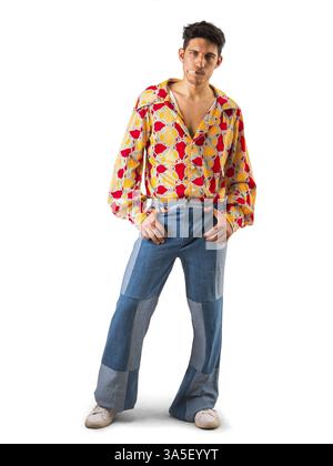 Voller Körper aus stilvollem jungen Männermodell in modischem Hemd mit buntem Druck und ausgestellter Jeans, rauchend Zigarette und Blick in die Kamera, isoliert Agave Stockfoto