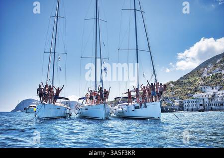 Viele Touristen stehen auf Segelbooten, die an sonnigen Sommertagen auf dem plätschernden Meerwasser in der Nähe von Berghängen mit Gebäuden unter blauem Himmel schwimmen Stockfoto