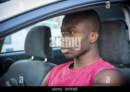 Handsome Young Black Mann Auto fahren, rotes Hemd tragen Blick auf die Straße vor ihm Stockfoto