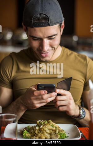 Seitenansicht eines hübschen jungen Mannes, der ein Foto von seinem Essen im Restaurant macht. Vertikale Innenaufnahme Stockfoto