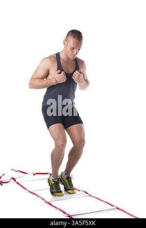 Attraktiver, sportlicher junger Mann, der mit einer Agilitätsleiter auf weißem Hintergrund arbeitet und nach unten blickt Stockfoto