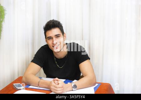 Attraktive lächelnden jungen Menschen studieren oder arbeiten zu Hause sitzen am Tisch mit Papier vor ihm Stockfoto