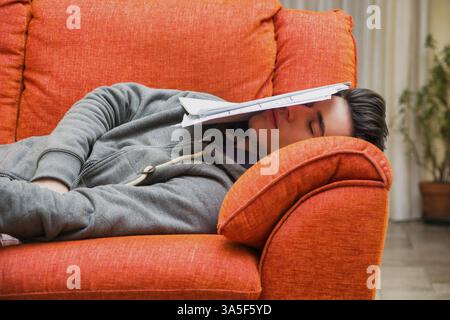 Über-arbeitete, müde Junge Mann zu Hause schlafen anstatt zu arbeiten oder studieren, ruht mit Kopf von Papier abgedeckt Stockfoto