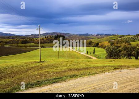 Wunderschönes Italien. Malerische Hügel der legendären Toskana. Flache Reihen von gepflügten Feldern und Wiesen. Unbefestigte Straße führt durch die Hügel. Das Konzept o Stockfoto