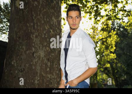 Attraktive junge Mann im Park neben Bäumen, wegschauen, eine Seite Stockfoto