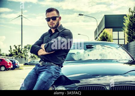 Porträt von brutalen bärtigen Jüngling in Sonnenbrille mit verschränkten Armen stützte sich auf seine polierte Neuwagen im freien Stockfoto
