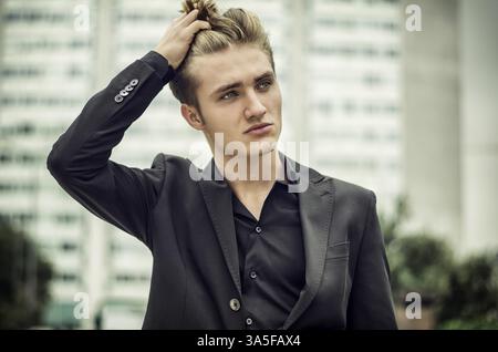 Ernst oder traurig blonden jungen Mann in Jeans und Jacke, sitzen im Freien auf der Suche in der Kamera Stockfoto