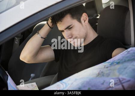 Nahaufnahme der wunderschöne junge Mann, der das Auto fährt, eine Karte hält, die verwirrt und verwirrt ist, wohin man gehen soll Stockfoto