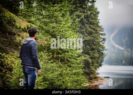 Schöner Yung-Mann, der auf dem Hintergrund des Waldes am Ufer des Sees steht und wegblickt Stockfoto