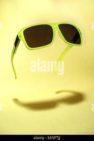 Helle grüne Farbe Sonnenbrille in der Luft. Grüne, die in der Luft schweben Sonnenbrille auf gelben Hintergrund. Untere Schatten unterhalb der Gläser. Minimalismus summ Stockfoto