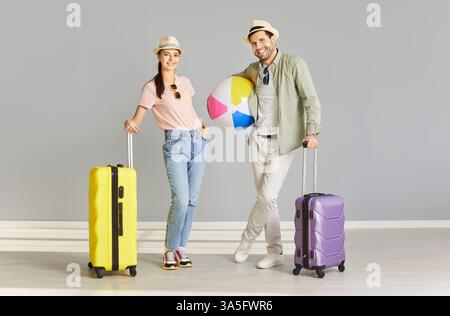 Familienpaar, das bereit ist, Sommerferien am Meer zu verbringen, mit Koffern und Strandball posiert Stockfoto