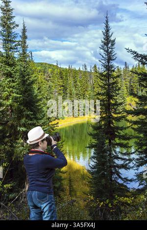 Eine Frau mittleren Alters mit einem schönen Hut macht Fotos vom See. Nördliche Kordillere. Kalter bewölkter Herbsttag. Die Northern Rocky Mountains. Der Tiefenbereich Stockfoto