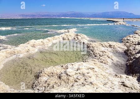 Israelische Küste des Toten Meeres. Das verdampfte Salz ragt über das Wasser hinaus. Windiger Frühlingstag. Die rosafarbenen Berge der jordanischen Küste Stockfoto