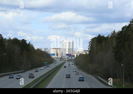 Eine geschäftige Autobahn in Jekaterinburg, Russland, mit Autos, umgeben von Bäumen und modernen Hochhäusern in der Ferne. Stockfoto