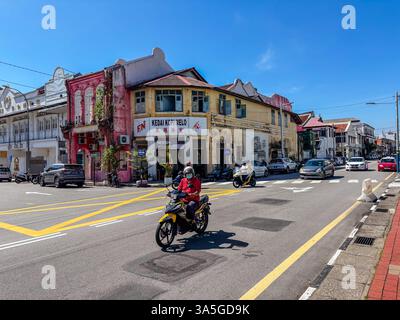 Eine typische Straße in George Town, Penang, Malaysia, mit farbenfrohen Kolonialgebäuden, Motorrädern und Autoverkehr an einem sonnigen Tag. Stockfoto