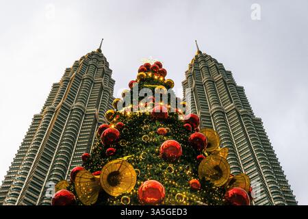 Kuala Lumpur, Malaysia: Ein atemberaubendes Niedrigwinkelbild eines wunderschön verzierten Weihnachtsbaums zwischen den Petronas Twin Towers Stockfoto