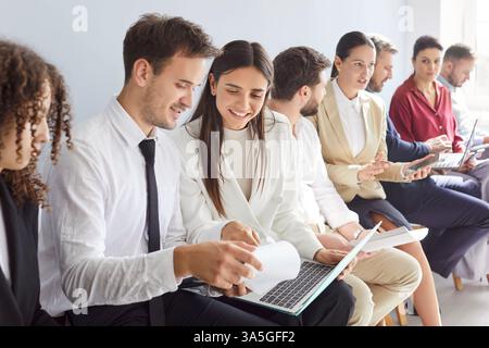 Junge Geschäftsleute, die in einer Reihe sitzen und während eines Meetings zusammen mit dem Laptop arbeiten Stockfoto