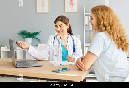 Glückliche junge Ärztin und Patientin, die auf Laptop-Computer blickt und lächelt Stockfoto