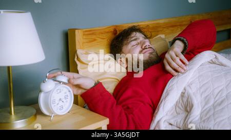 Mann hat Schwierigkeiten, aufzuwachen – Schlummerschlag auf Wecker Stockfoto