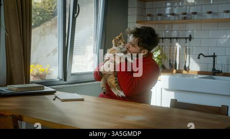 Ein glücklicher junger Mann hält seine entzückende Katze in einer hellen und gemütlichen Küche und genießt einen verspielten und entspannenden Moment zu Hause Stockfoto