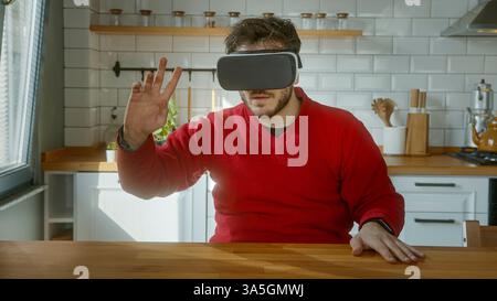 Junger Mann, der in ein aufregendes Virtual Reality-Erlebnis eingetaucht ist, ein High-Tech VR-Headset trug und aktiv mit der digitalen Welt in einer modernen Welt interagierte Stockfoto