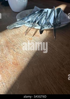 Vier Bestecksets auf einem Teller auf einem Holztisch in einem Restaurant mit einer leichten Sonneneinstrahlung Stockfoto