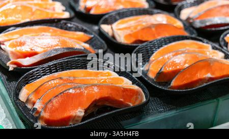 Frische Lachssteaks, die in schwarzen Körben auf Eis angeordnet sind, präsentieren sich in leuchtender Farbe und hoher Qualität und können auf einem Fischmarkt verkauft werden Stockfoto