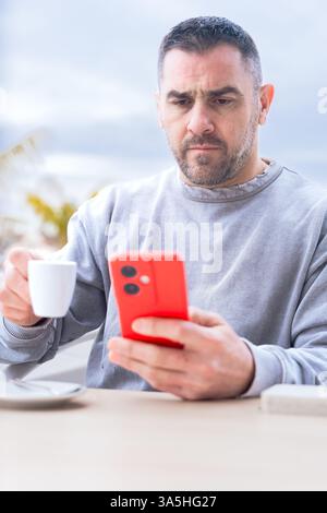 Ernsthafter Mann ernst, während er in einem Café im Freien auf ihrem Smartphone tippt. Stockfoto
