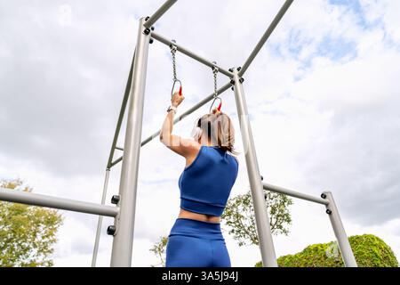 Niederwinkelrückansicht einer sportlichen jungen Frau mit Turnringen in einem Outdoor-Fitness-Park. Stockfoto