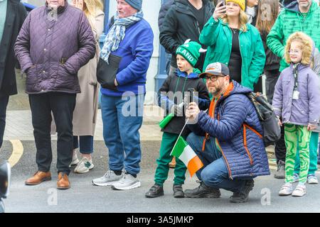 St. Patrick Parade. Arklow, Irland. 2025 Vater und Sohn genießen die St. Patrick’s Day-Parade, bei der Erinnerungen in einer lebendigen, festlichen Menge festgehalten werden. Stockfoto