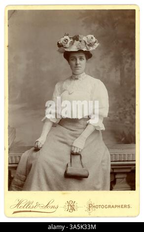 Originale edwardianische Schrankkarte der hübschen edwardianischen Frau, edwardianischen Dame, die Mode im Frühling oder Sommer trägt - eine weiße Bluse aus Leinen und Spitze, weiße Handschuhe aus Spitze, ein Hut mit Rosen, eine kleine Handtasche in der Hand, Studio of Hellis & Sons Photographers, London, datiert vom Juli 1907 auf der Rückseite. Stockfoto