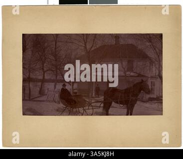 Ein historisches Foto von Oma Pierce (Alice) George in einem Pferdeschlitten, mit einem Haus und einem Mann auf der Veranda in Mankato, Minnesota. Stockfoto