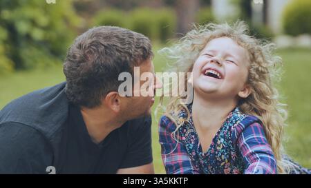 Vater lacht zusammen mit Tochter während des sonnigen Parkspaziergangs und genießt spielerische Bindungsmomente mit echtem Familienglück Stockfoto
