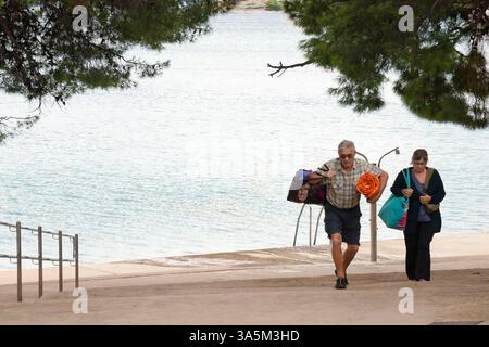 Tribunj, Kroatien - 14. September 2024: Reife Ehepaare gehen außerhalb der Saison vom leeren Strand weg Stockfoto