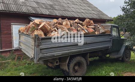Ein alter Truck mit Feuerholz in der Nähe eines Holzhauses auf dem Land Stockfoto