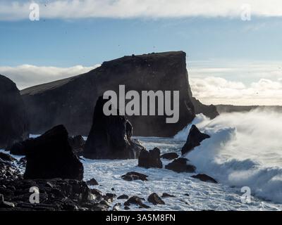 An der zerklüfteten Küste von Valahnúkamöl sind riesige Basaltmeerstapel und steile Klippen zu sehen, während mächtige Atlantikwellen gegen die Vulkanküste cre krachen Stockfoto