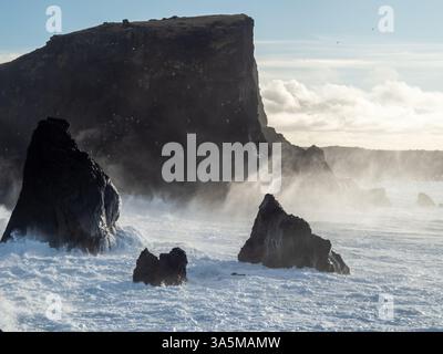 Wellen brechen bei Valahnúkamöl gegen zerklüftete Vulkangesteine und senden Nebel in die Luft. Hoch aufragende Klippen und dunkle Meeresstapel schaffen ein dramatisches, ungezähmtes C Stockfoto