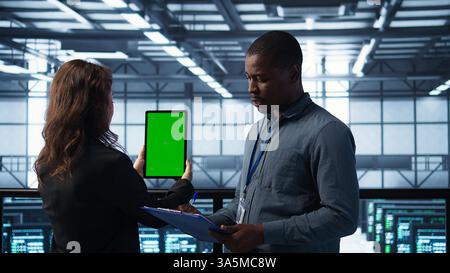 Techniker im Rechenzentrum, die ein Tablet mit grünem Bildschirm verwenden und die Hardwarediagnose überprüfen. IT-Mitarbeiter passen Serverkonfigurationen mithilfe eines Modellgeräts an, wenden Firmware-Updates an, Kamera B Stockfoto
