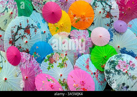 Eine lebendige Auswahl an farbenfrohen asiatischen Papierschirmen mit Blumenmotiven, die sich bei Nahaufnahme überlagern Stockfoto