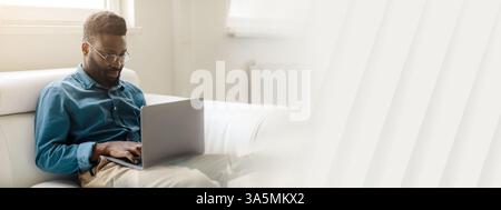 Junger afroamerikanischer Geschäftsmann, der Aufgaben mit Laptop im Büro verwaltet Stockfoto