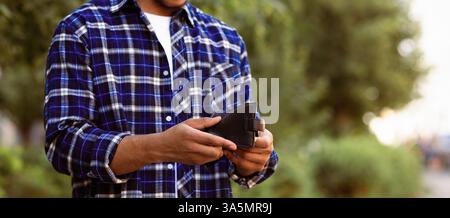 Zugeschnittenes Bild von schwarzem Kerl Blick auf seine leere Geldbörse Stockfoto