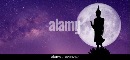 A silhouette of a Buddha statue stands peacefully under the full moon, with the Milky Way stretching across the night sky. The concept of spirituality Stockfoto